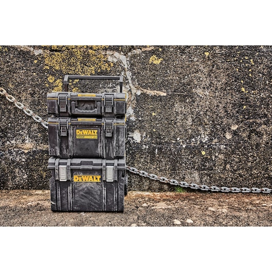 Three stacked DEWALT ToughSystem 2.0 toolboxes are positioned outdoors against a textured concrete wall with yellow speckles