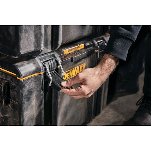 Hand opening latch on a DEWALT ToughSystem 2.0 storage box in a workshop setting.