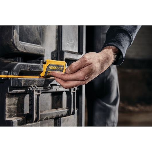 Hand operating the yellow TOUGHSYSTEM latch on a DEWALT storage box in a workshop setting.