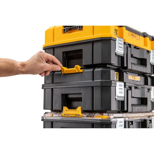 Hand unlocking yellow latch on stacked DEWALT toolboxes with black and yellow design.
