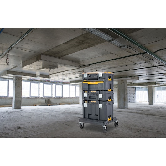 Stacked DEWALT toolboxes on wheels in an unfinished concrete building with large windows.