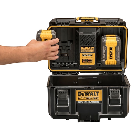 A DEWALT ToughSystem 2.0 18V Charger Toolbox is shown open. The inside of the lid features a mounted battery charger and two DEWALT batteries. A hand is placing a battery into the charger. The lower compartment is empty, and the toolbox has durable latches and a yellow and black color scheme.