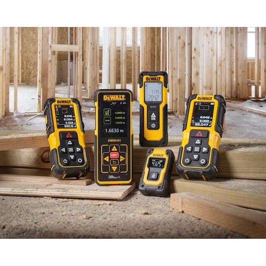 Several DEWALT laser distance measuring devices are displayed on wooden beams at a construction site with exposed framing in the background.