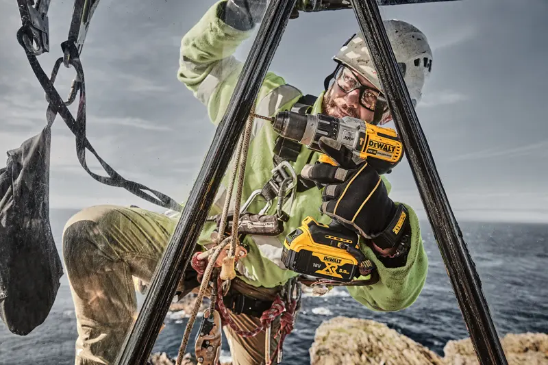 Photo of worker using DEWALT drill, SKUs DCD996P2, DCD996P2-QW, outdoors with safety gear near sea.